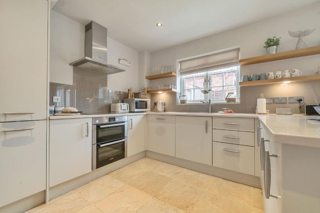 une grande cuisine avec des armoires blanches et une fenêtre dans l'établissement Curlew Cottage, à Brancaster