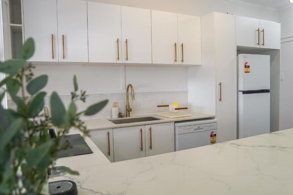 a kitchen with white cabinets and a sink and a refrigerator at Seeside Cottage - See St Bargara in Bargara