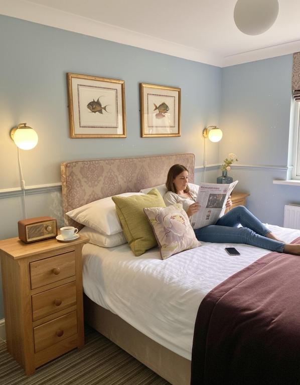 a woman sitting on a bed reading a newspaper at The Emsworth in Emsworth