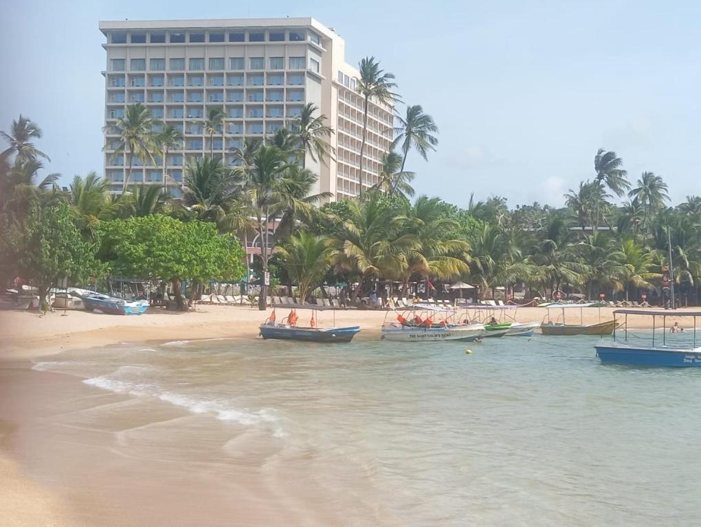 a beach with boats in the water and a building at Sun Terra Unawatuna in Unawatuna