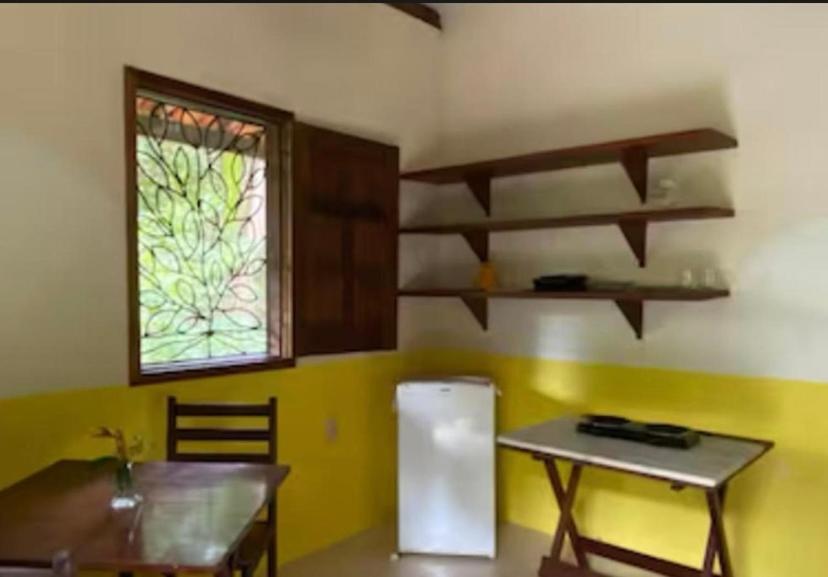 a kitchen with a table and a refrigerator and a window at Garden House in Ilha de Boipeba