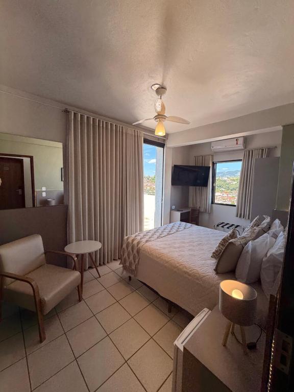 a bedroom with a bed and a chair and a window at Hotel Ze Maria Cambui in Cambuí