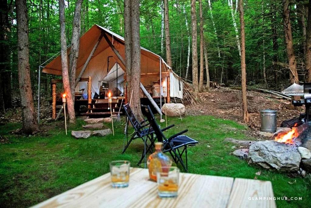 a tent in the woods with a table and a fire at Rustic Safari Tent for a Unique Glamping Experience near Gore Mountain, New York in North Creek