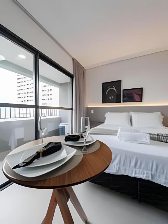 a white bedroom with a large bed and a wooden table at Studio Elegante - USP, Metrô Butantã e Acadepol in São Paulo