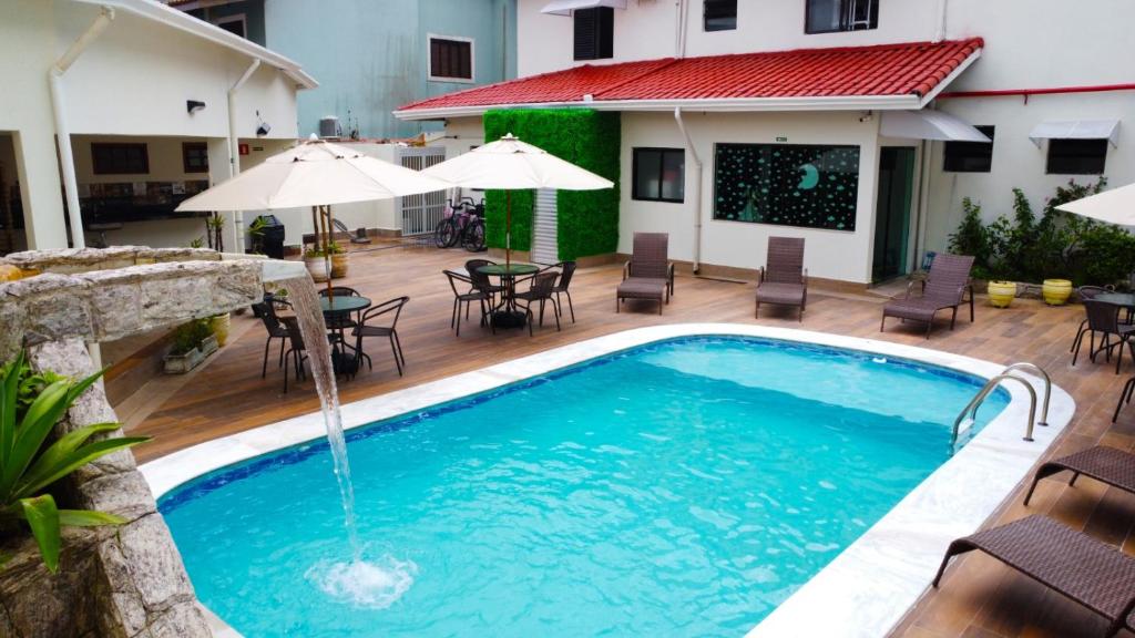 una piscina con sillas, mesas y sombrillas en Pousada Apatej, en Peruíbe