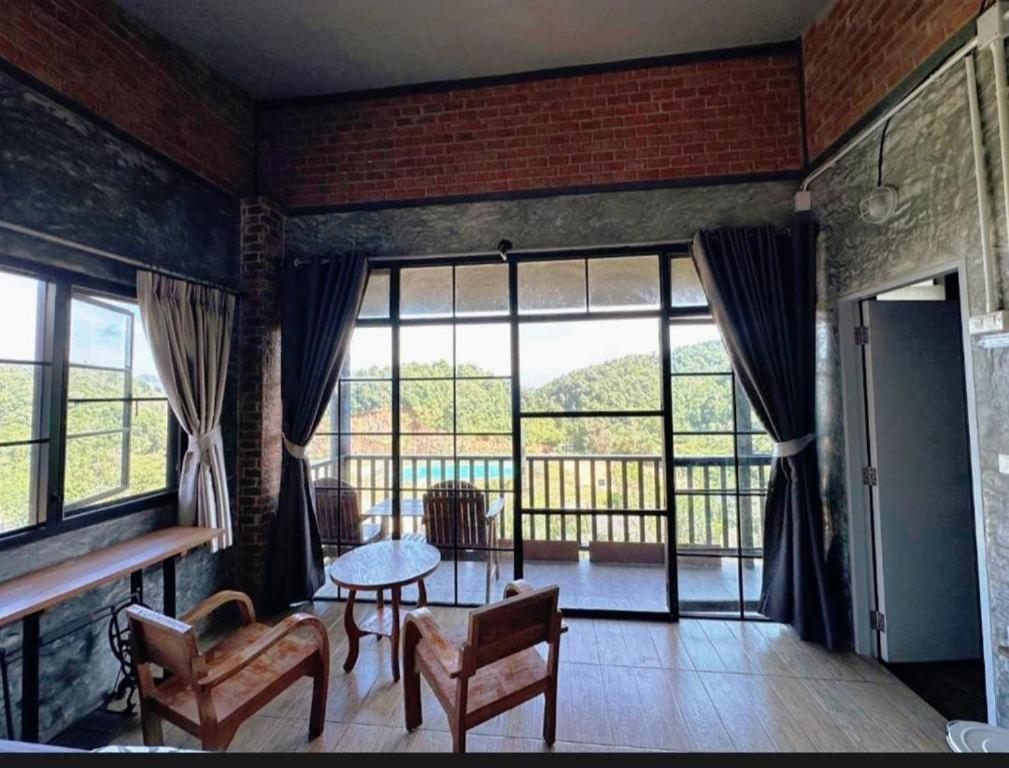 ein Wohnzimmer mit Tisch und Stühlen und Fenstern in der Unterkunft pilokhillhouse บ้านอีต่องเหมืองปิล็อก in Ban Pilok Khi