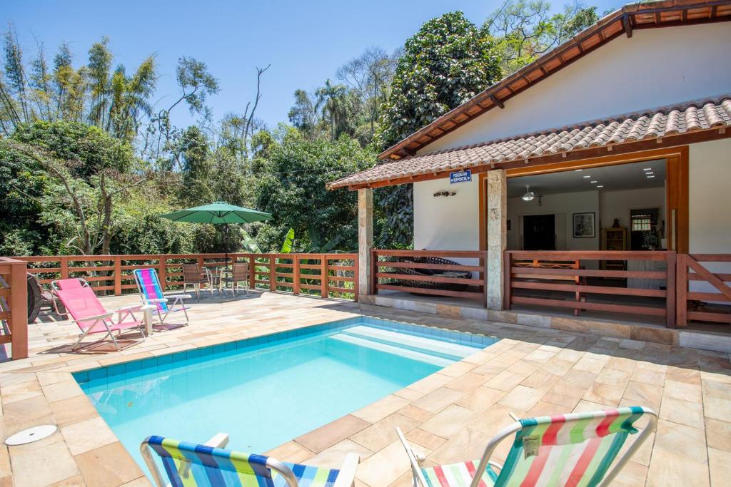 a pool with chairs and an umbrella next to a house at Sitio com Piscina, Jogos e Espaco Home Office in Cinco Lagos