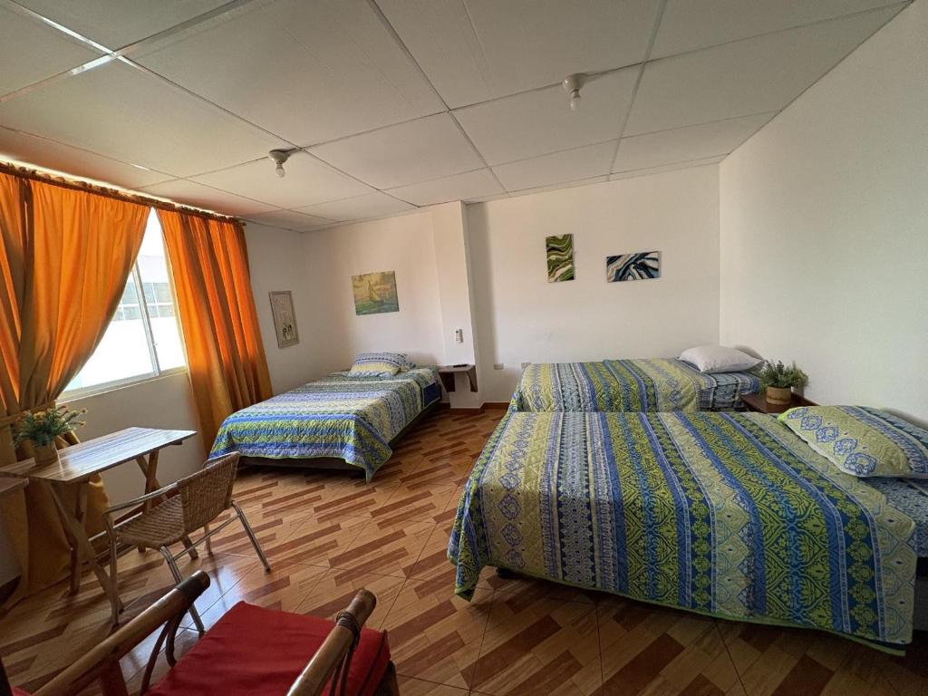 a room with three beds and a table and a desk at Hostal Shaddai in Manta