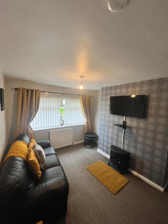 a living room with a leather couch and a television at 100 Castle in New Cumnock