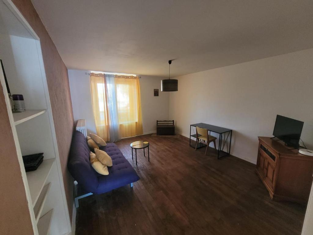 een woonkamer met een blauwe bank en een televisie bij Appartement Jarny proche gare in Jarny