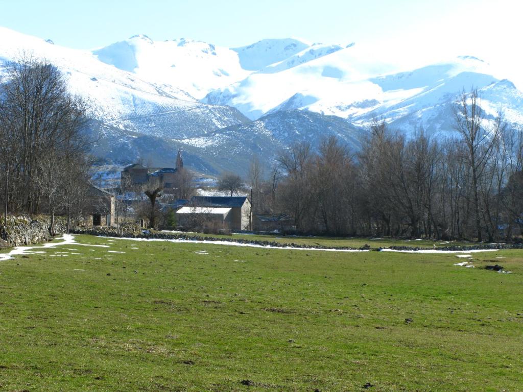 a field with a house and a snow covered mountain at Casa La Farrapona de Babia in Torrestío