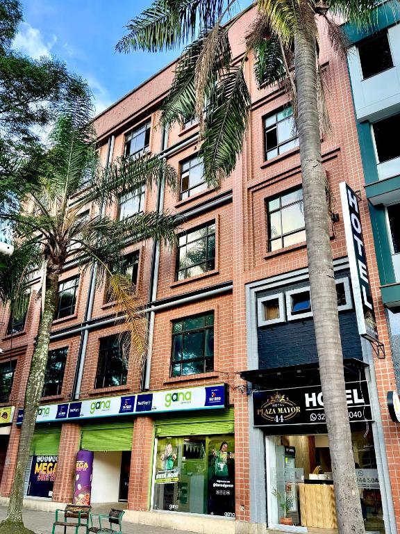 a red brick building with palm trees in front of it at Hotel Plaza Mayor 44 in Medellín