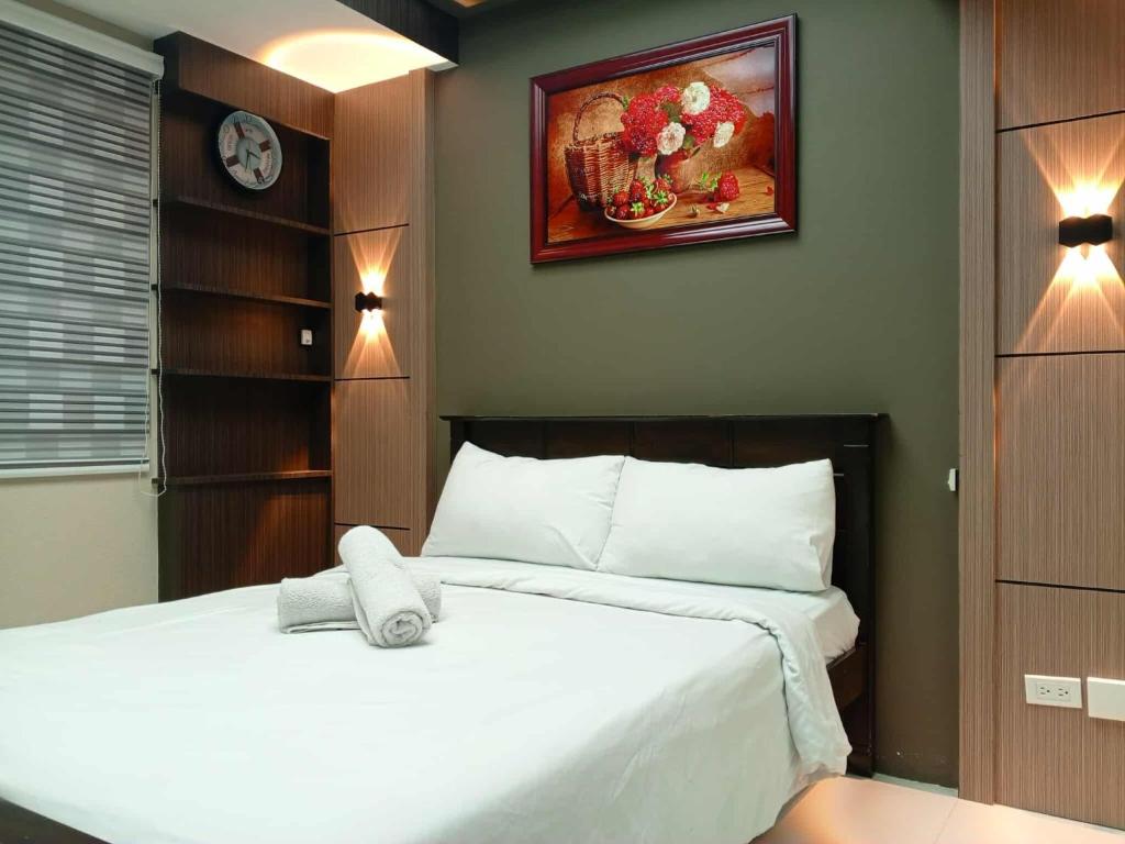 ein Schlafzimmer mit einem weißen Bett mit einer Uhr an der Wand in der Unterkunft Cozy Manila Condo Retreat with Shared Pool in Manila