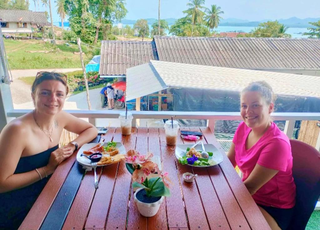 Ein Mann und eine Frau sitzen an einem Holztisch mit Essen in der Unterkunft The white resort & restaurant koh yao yai in Ban Khlong Hia