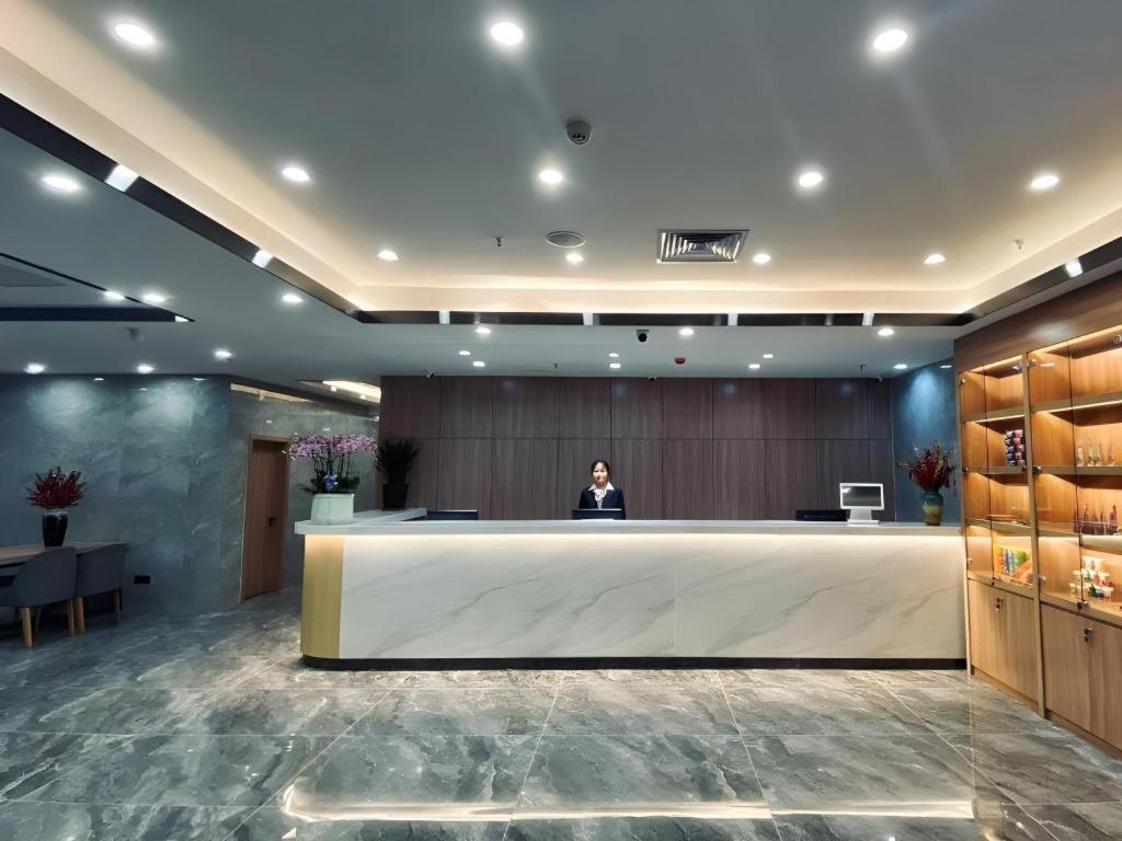 a man standing behind a large reception desk in a lobby at Shell Hotel Shandong Jinan Daming Lake in Jinan
