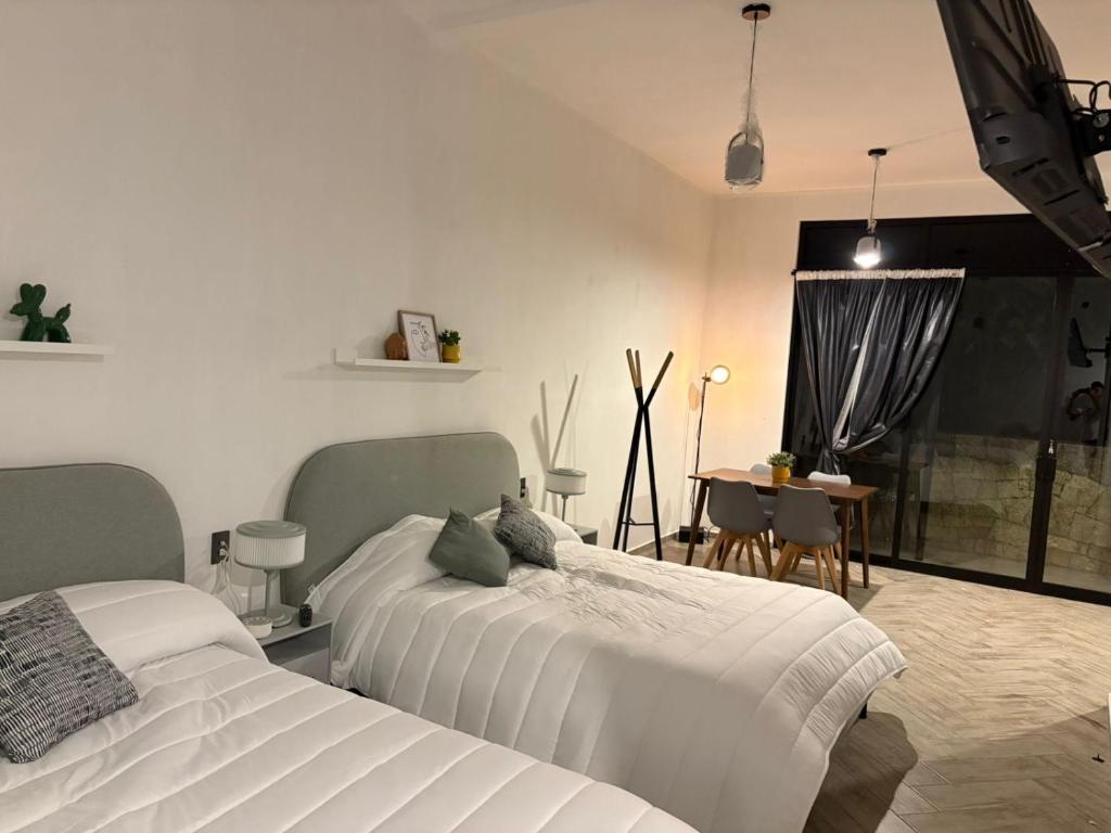 two beds in a white room with a table and a tableablish at Hotel ënxë habitación grande camas queen in Cuetzalán del Progreso