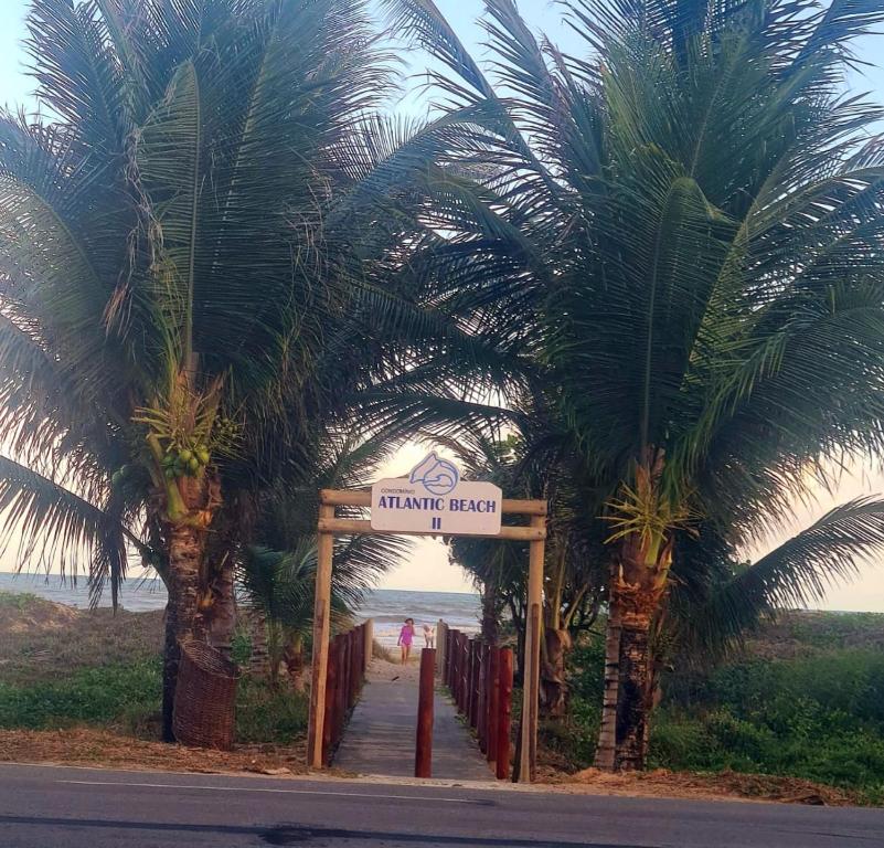 Un cartel que indica la entrada a una playa con palmeras en Casa cinza em frente à praia em condominio, en Aracaju