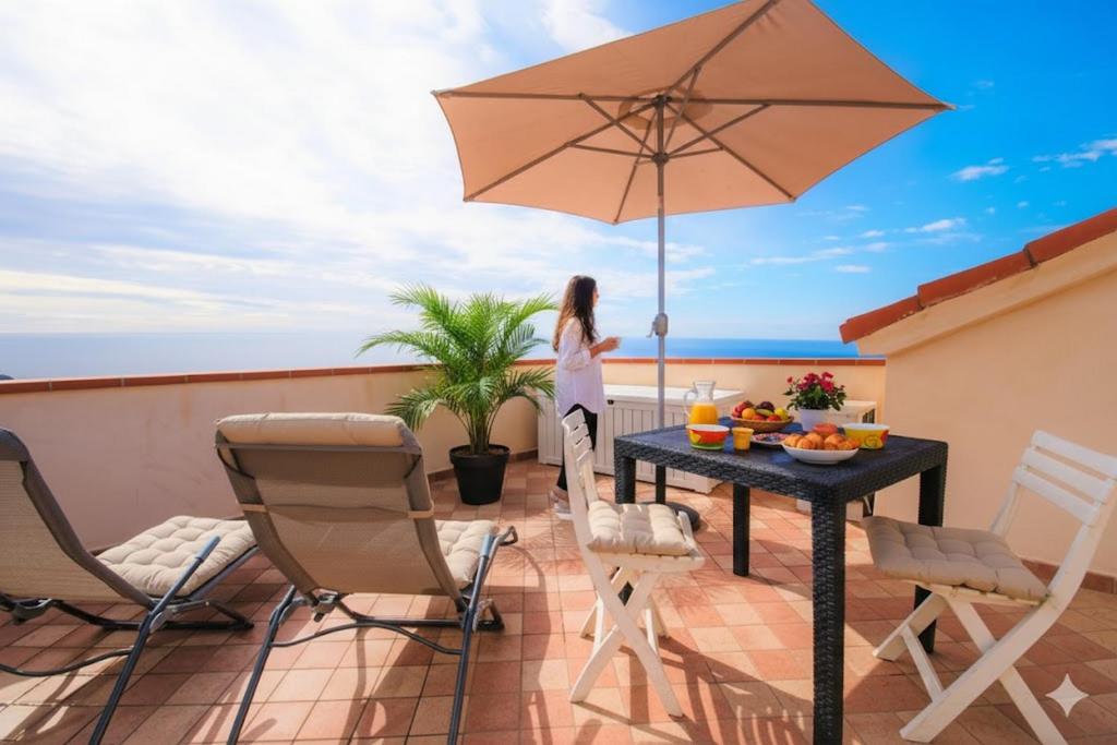 a woman standing on a balcony with a table and an umbrella at The Old Ship in Costarainera