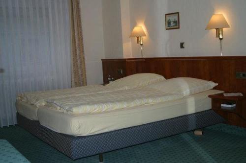 a bed in a hotel room with two lamps on the wall at Landgasthof Deutsches Haus in Ulmbach