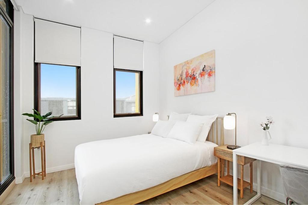 ein weißes Schlafzimmer mit einem Bett und zwei Fenstern in der Unterkunft Lumière Riverside One Bedroom Apartment In Ryde With Queen Bed and Free Parking Close to Train & Ferry & Cafes in Sydney