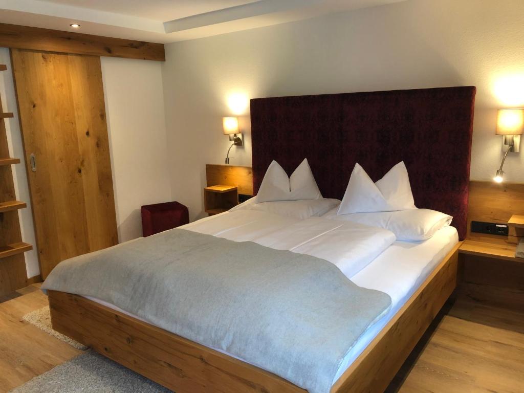 una habitación con una cama grande con sábanas y almohadas blancas en Hotel Garni Central - Zimmer - Studios - Apartments, en Kappl