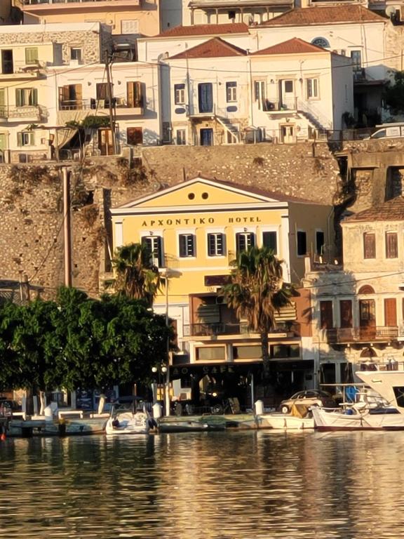 a yellow building with palm trees and boats in the water at Archontiko Hotel in Kalymnos