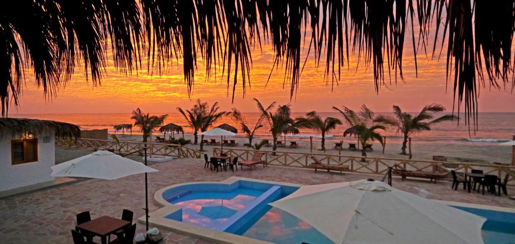 ein Sonnenuntergang am Strand mit Pool und Sonnenschirmen in der Unterkunft Palo Santo Blue Hotel in Zorritos