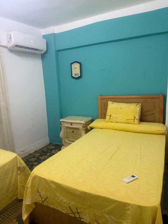 een slaapkamer met een bed met een gele sprei en een blauwe muur bij Roma apartment in Dumyat al Jadidah
