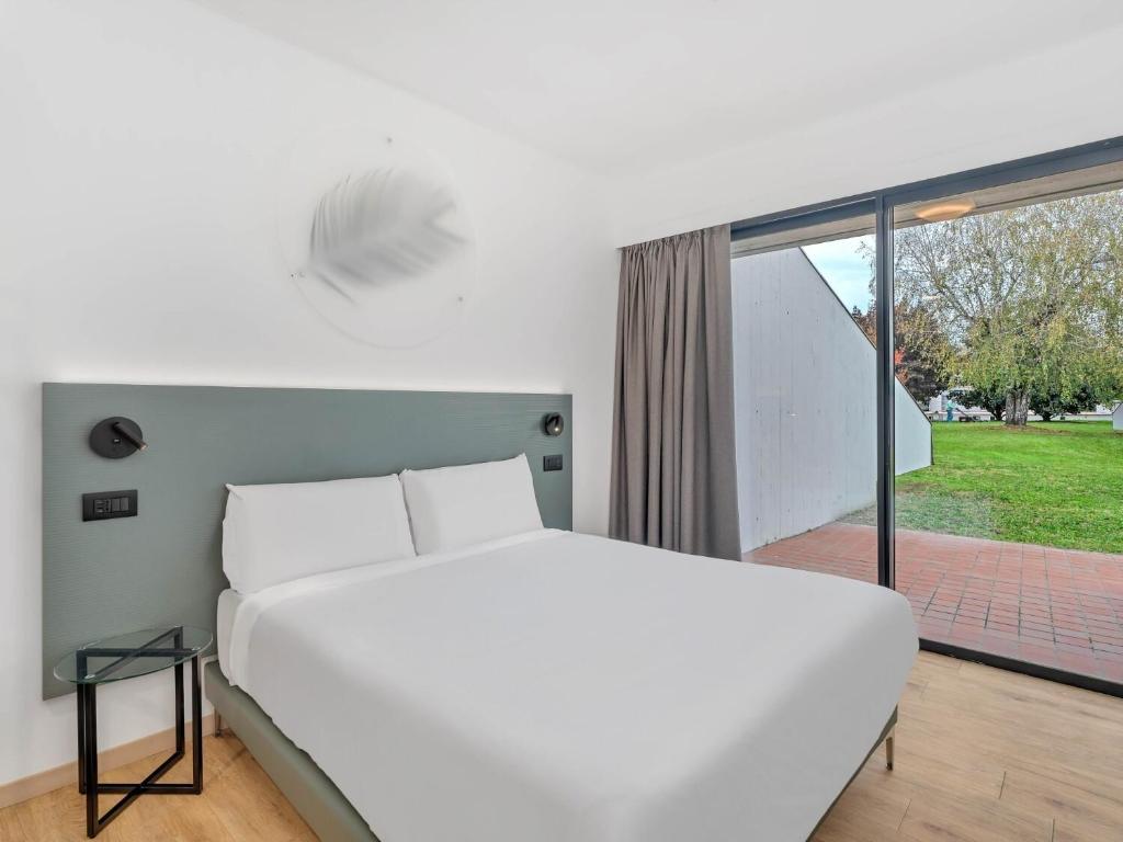 a bedroom with a white bed and a large window at B&B HOTEL Alba in Alba