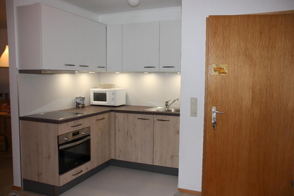 a kitchen with white cabinets and a microwave and a door at Lichtblick in Petersdorf auf Fehmarn