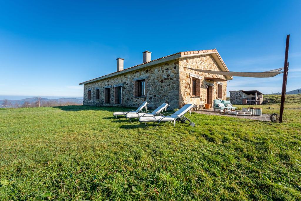 a stone house with lounge chairs in a field at Casona Alto Sarracin in Lloreda