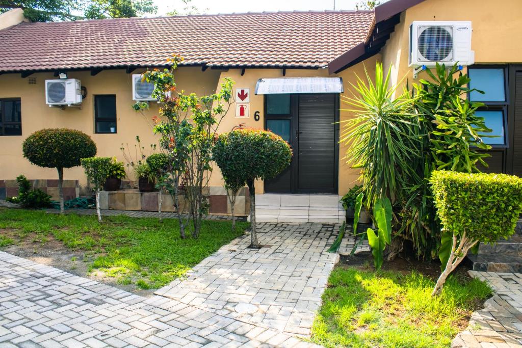 a yellow house with a black door and a brick driveway at Stopover lodge in Rustenburg