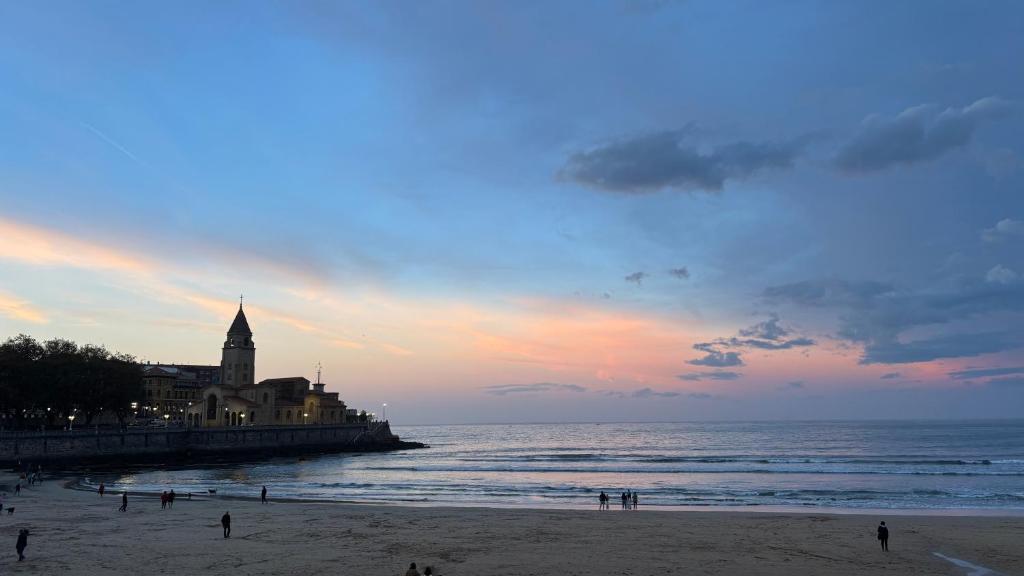 een strand met een klokkentoren en mensen op het strand bij Apartamento Playa de Gijon in Gijón