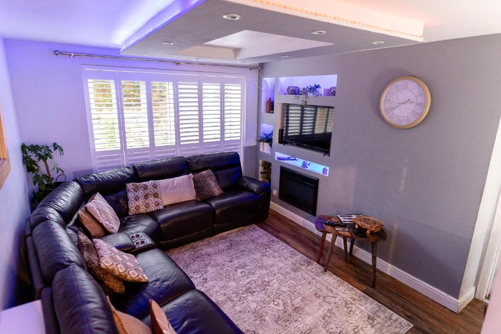 a living room with a leather couch and a clock at Sleeps 5 - Free Parking - Near Airport & City in Wythenshawe