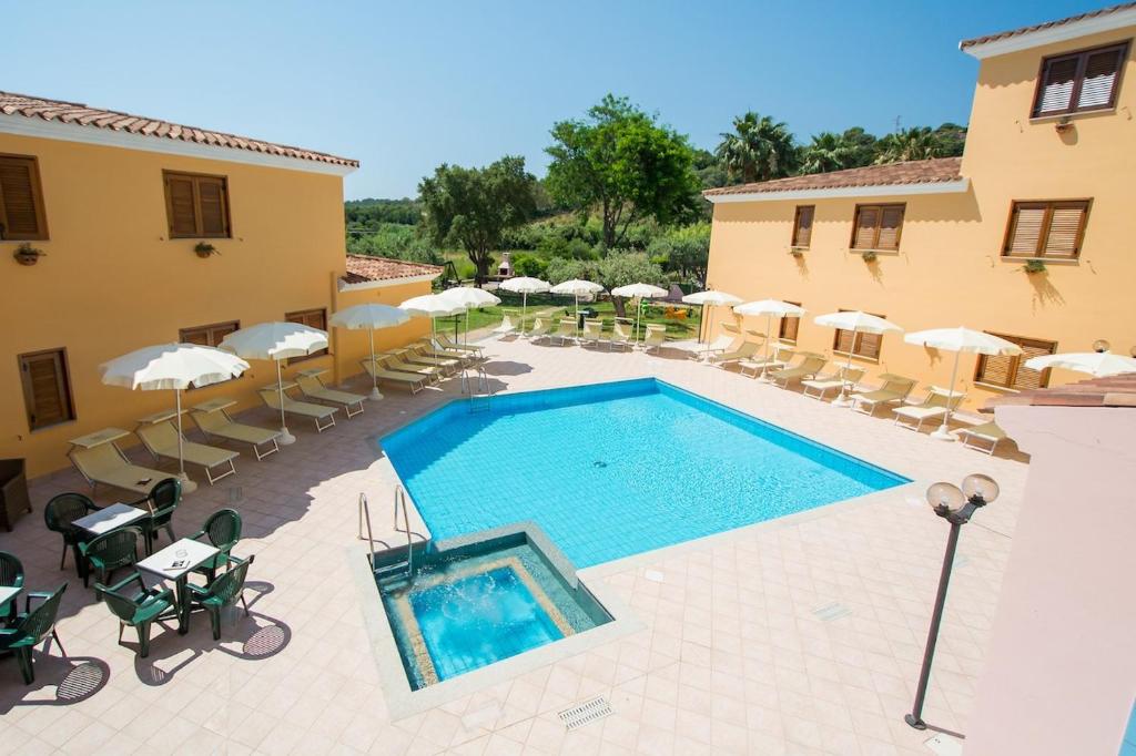 Una piscina con sillas y sombrillas al lado de un edificio. en Residence con piscina a Sos Alinos, en Cala Liberotto