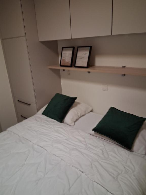 a white bed with two green pillows on it at Sailors' Park Villa Zephir in Nieuwpoort