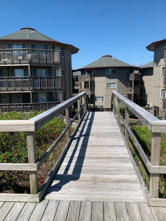 a wooden bridge over a beach with buildings in the background at Salty Sisters in Kill Devil Hills
