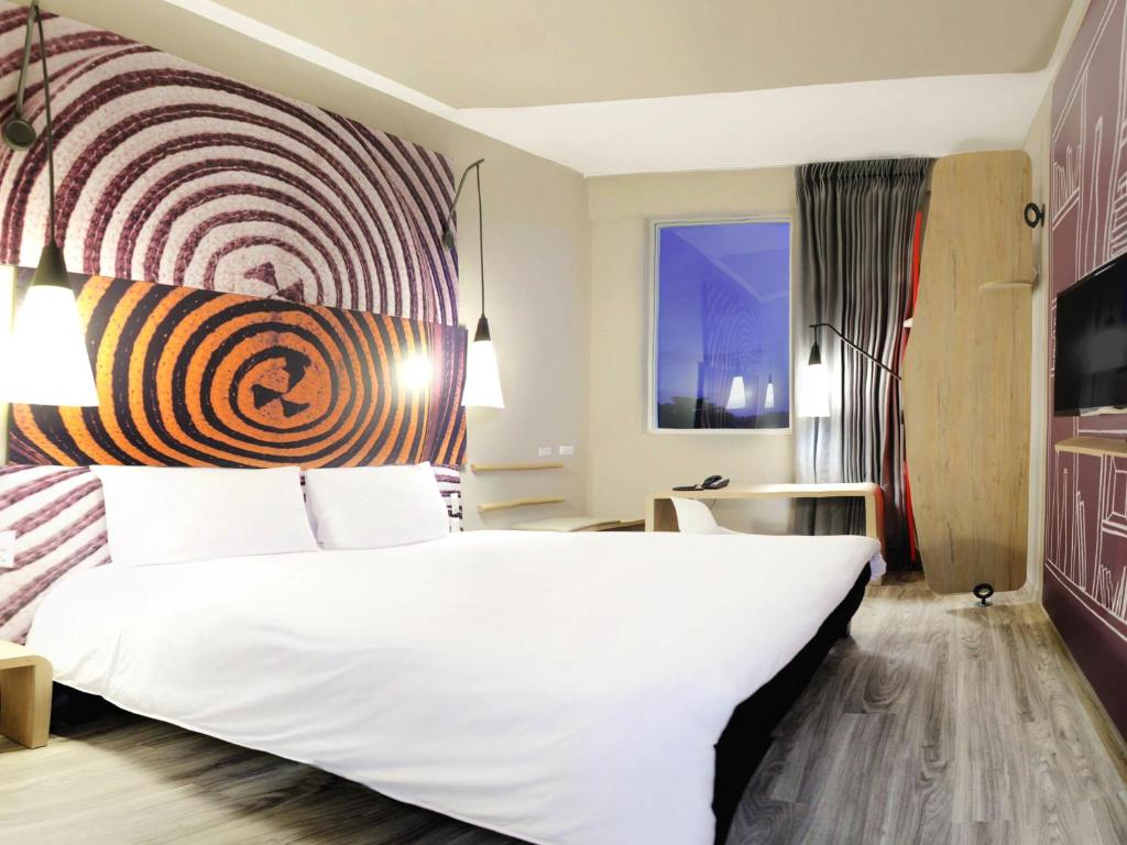 a bedroom with a large white bed with a colorful headboard at ibis Apartado in Apartadó