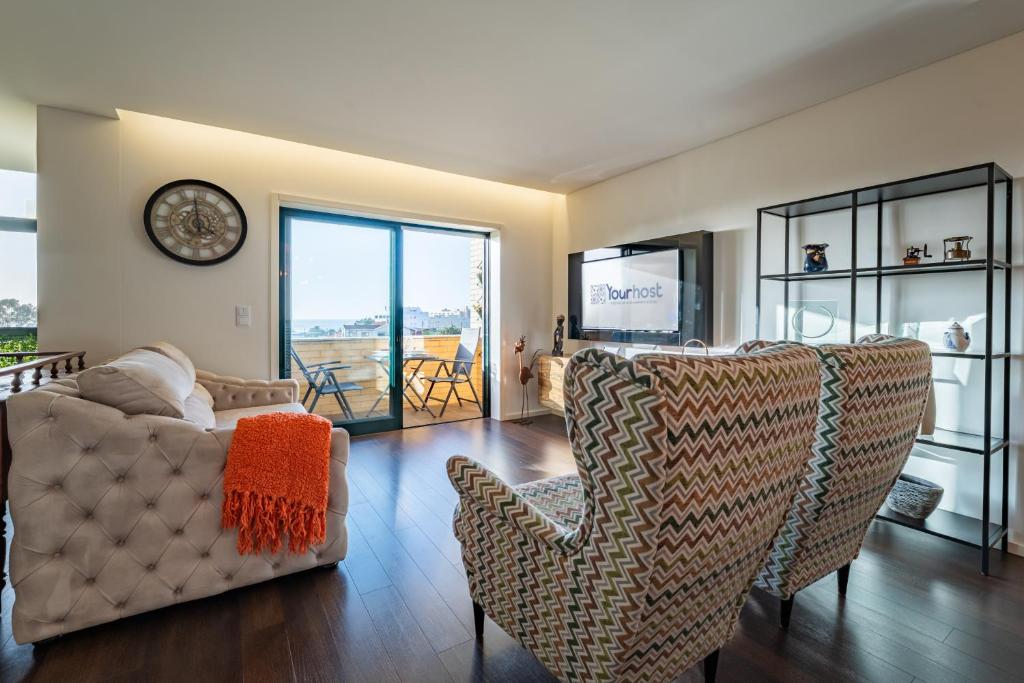 a living room with a couch and chairs and a clock at Sun, Sea, and Comfort Apartment in São Félix da Marinha