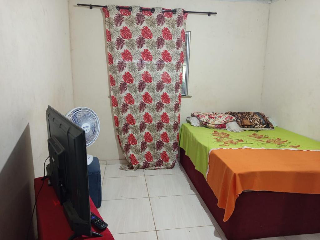 a bedroom with a bed and a tv and a curtain at Recanto Barcelos de Mel com piscina e churrasqueira in Camamu