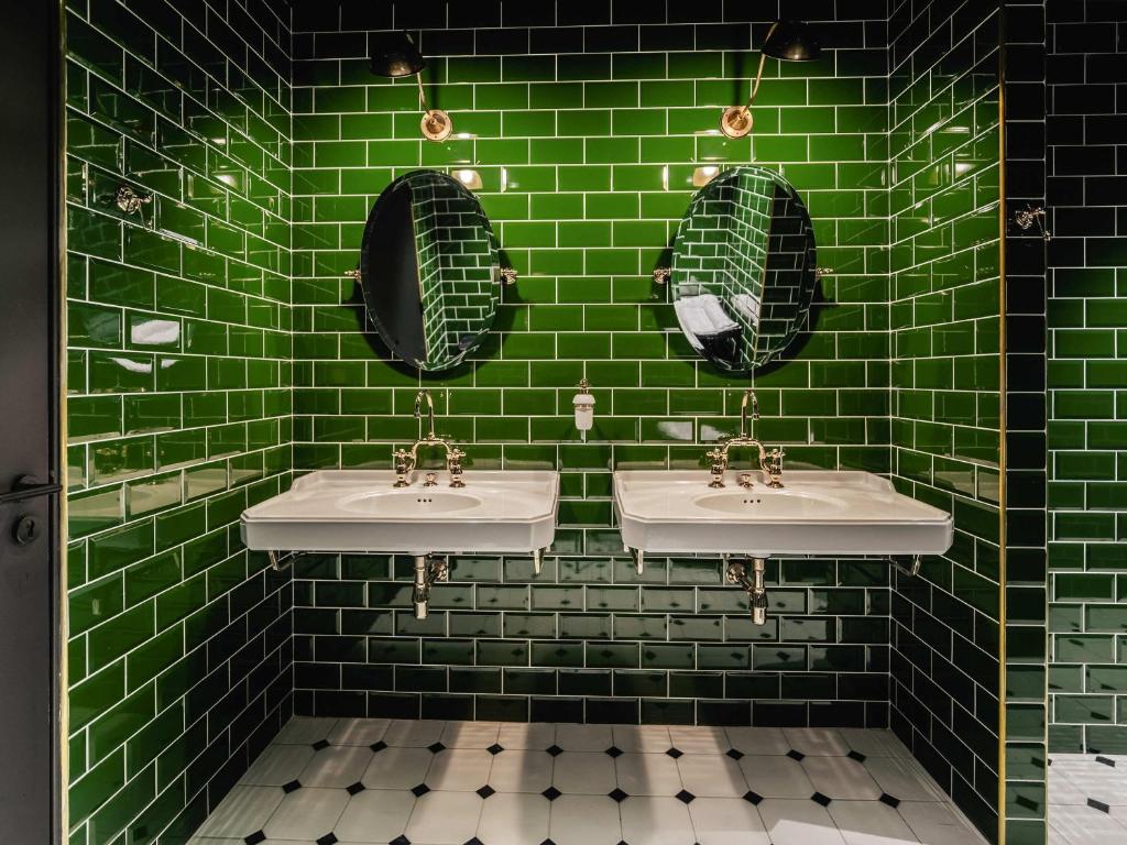 uma casa de banho em azulejo verde com 2 lavatórios e espelhos em ibis Styles Castelnaudary em Castelnaudary