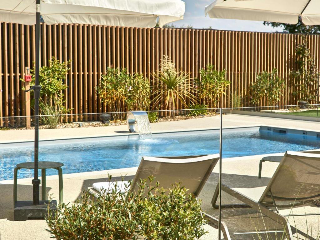 a swimming pool with two chairs and an umbrella at ibis Styles La Roche-sur-Yon in Mouilleron-le-Captif