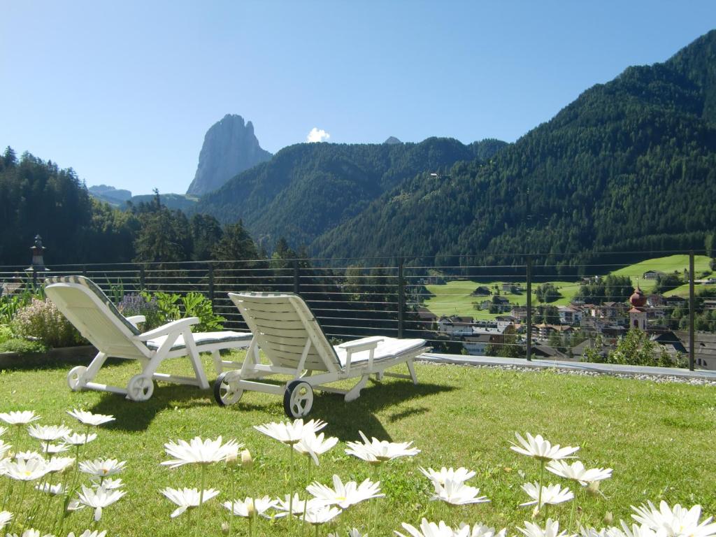 two chairs and flowers in the grass with mountains at Villa Quenz Family Suites in Ortisei