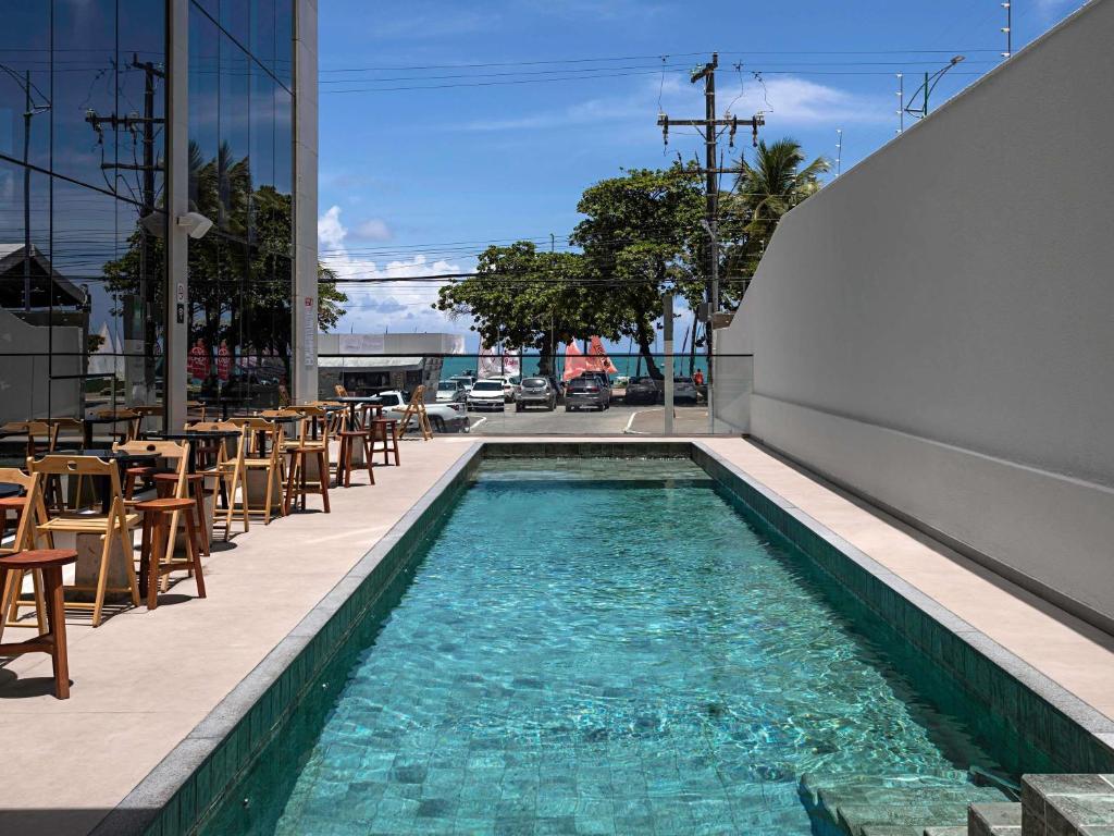 a swimming pool with tables and chairs on a building at ibis Styles Maceió Pajuçara in Maceió