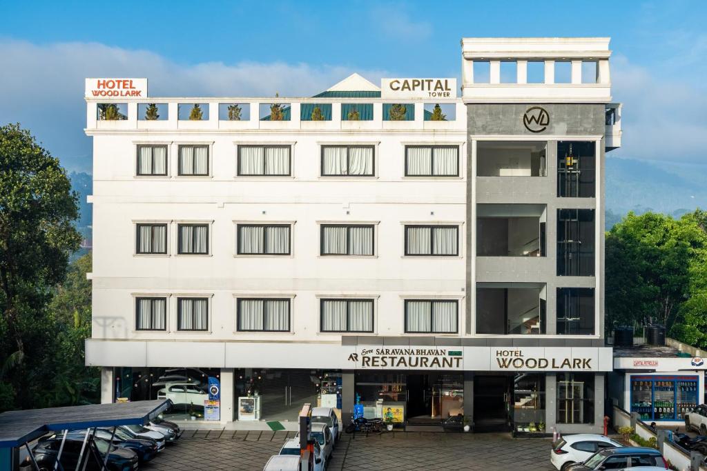 a white building with cars parked in a parking lot at Hotel Woodlark in Kattappana