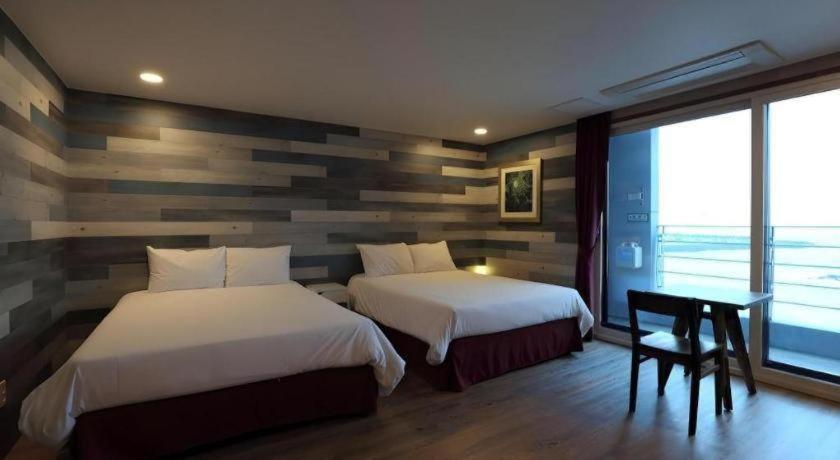 a bedroom with two beds and a desk and a window at HOTEL52 in Seogwipo