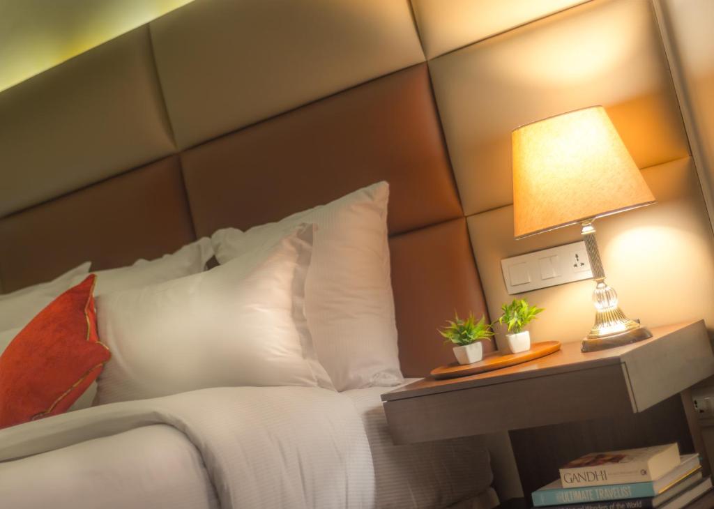 a bed with white pillows and a lamp on a table at Luxus Grand Hotel in Lahore