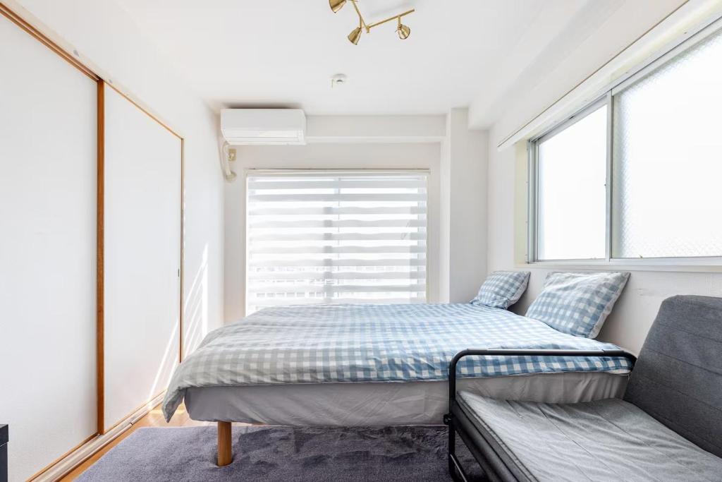 a bed and a couch in a room with windows at 湘南茅ヶ崎/湘南ライフの楽しめるアパートメント in Chigasaki