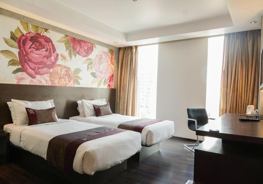 a hotel room with two beds and a desk at Akmani Hotel Jakarta in Jakarta