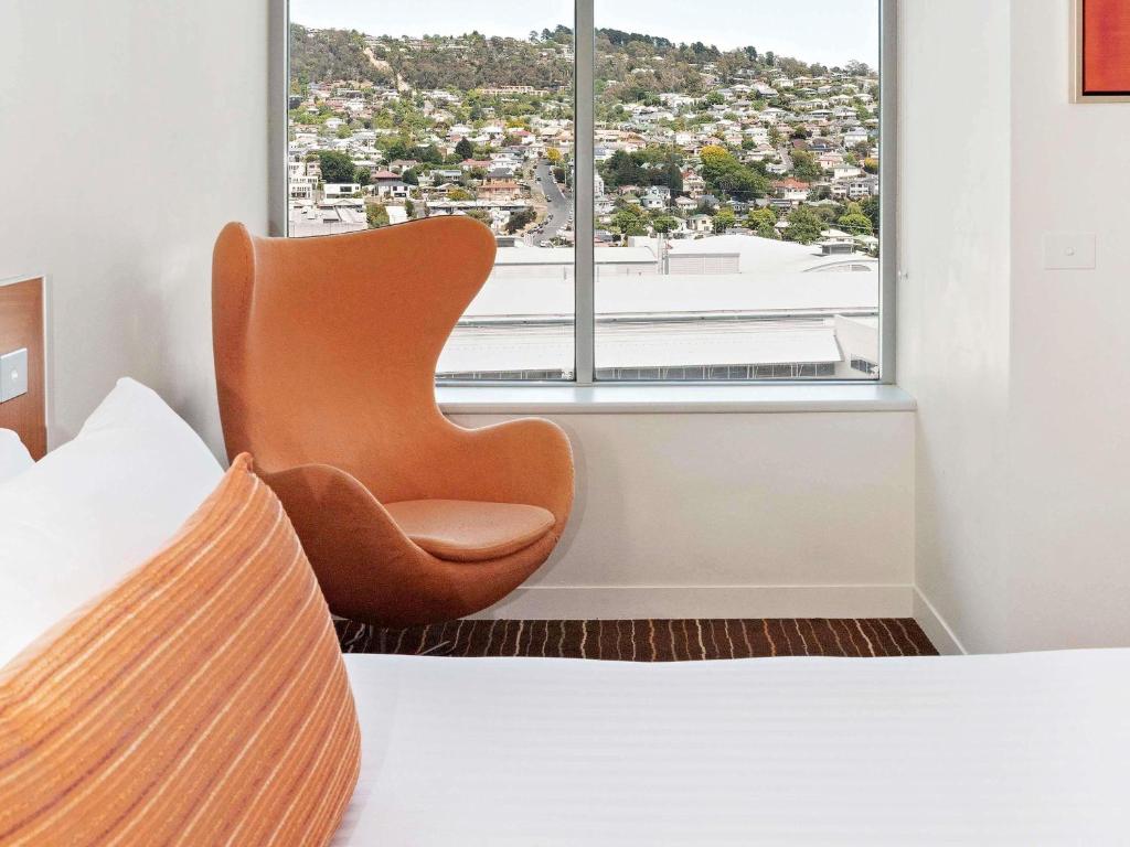 una silla sentada frente a una ventana en un dormitorio en Mantra Charles Hotel, en Launceston